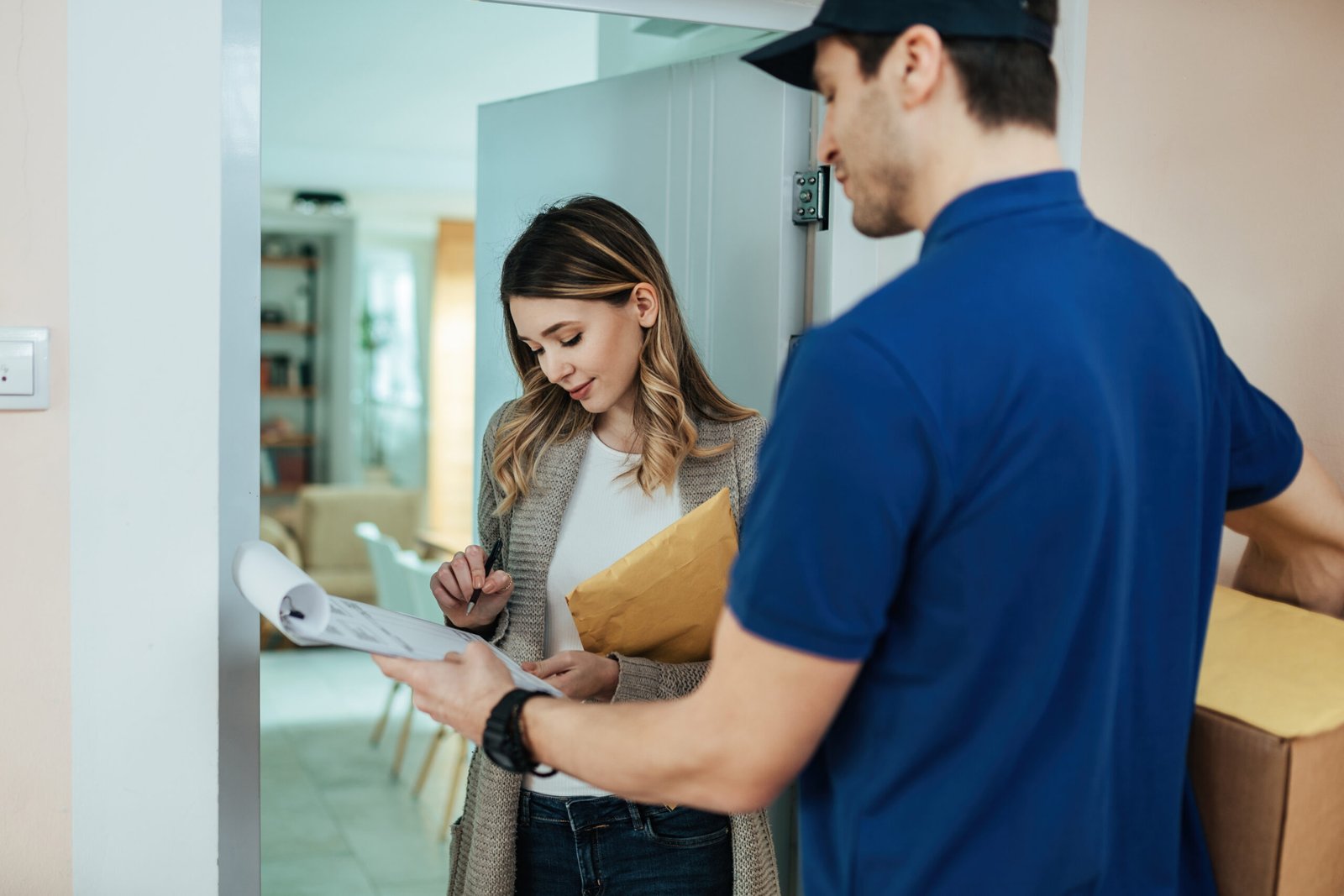 Young woman signing documents while receiving home delivery from a courier.